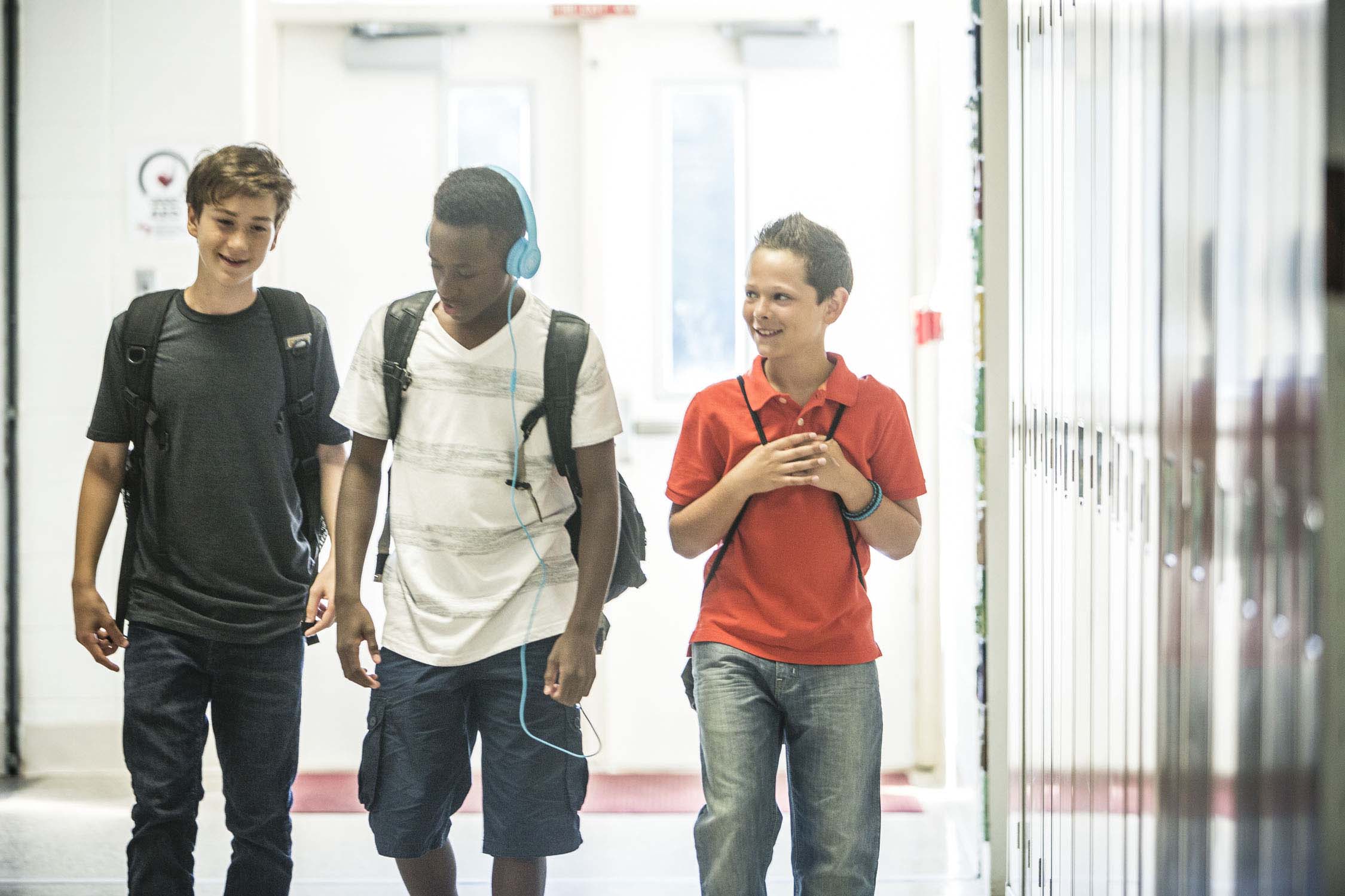 three teen boys walking in school hallway